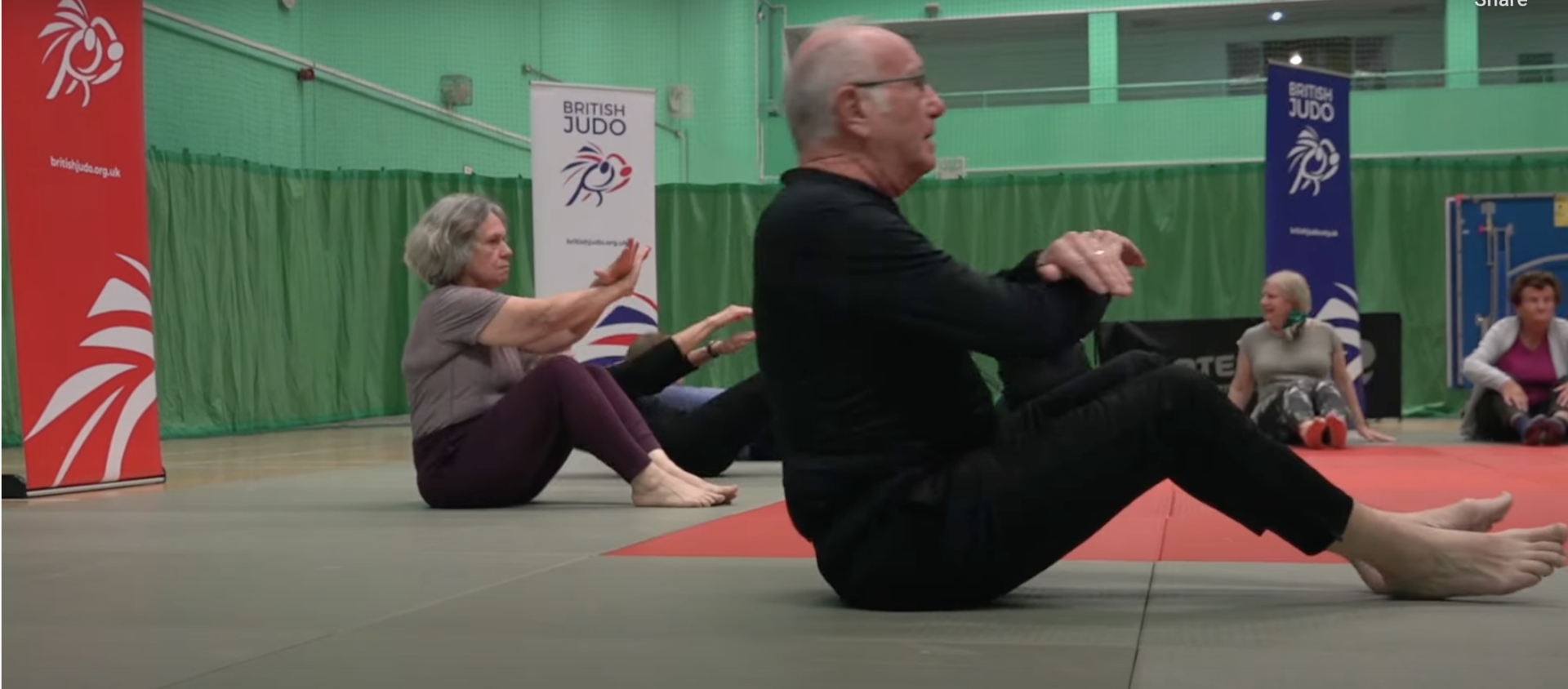 Image of a man and three women, sitting down on judo tatami with their arms crossed about to do a backwards breakfall, each person is over 60 years old